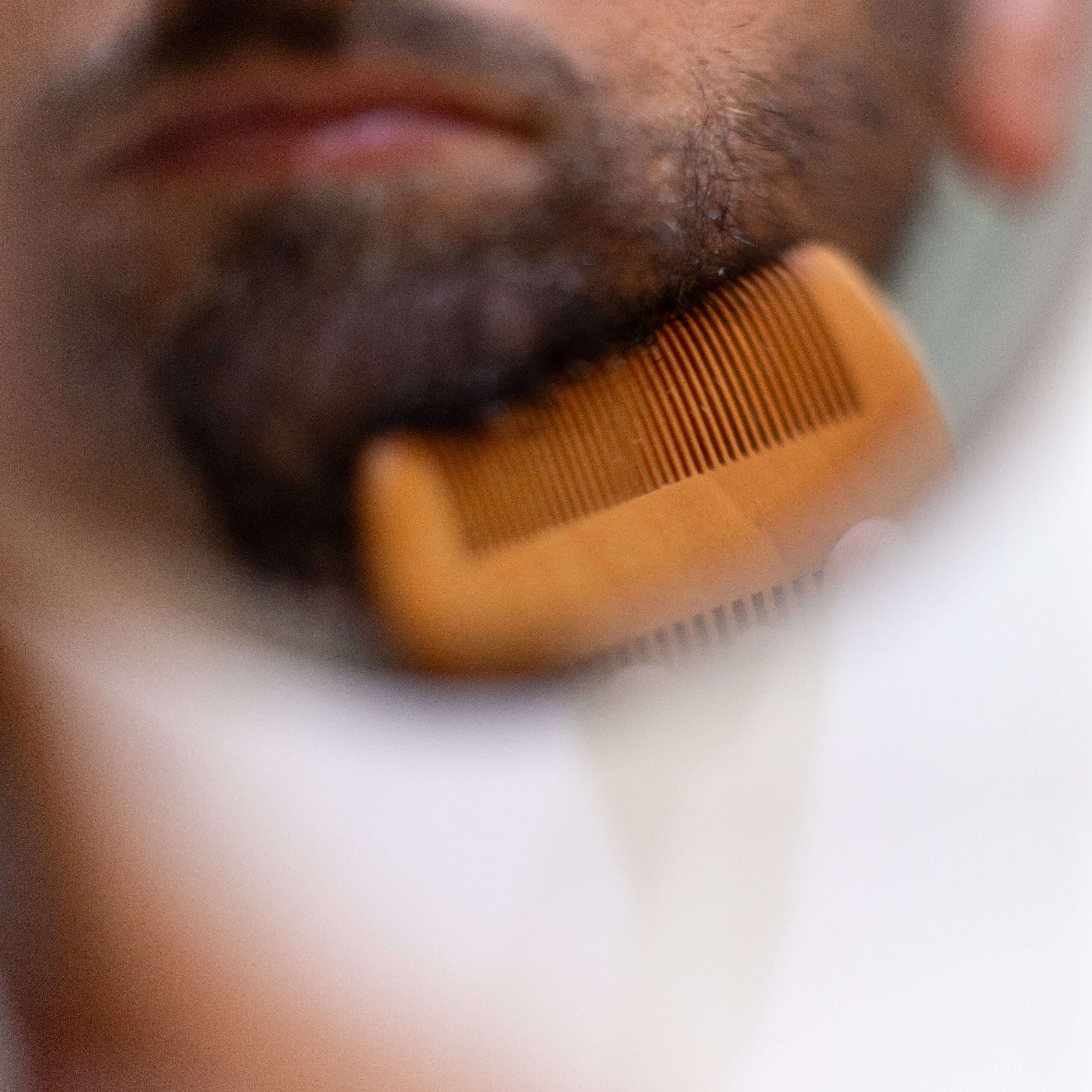 Man grooming beard with wooden comb, maintaining a soft and dense beard naturally.