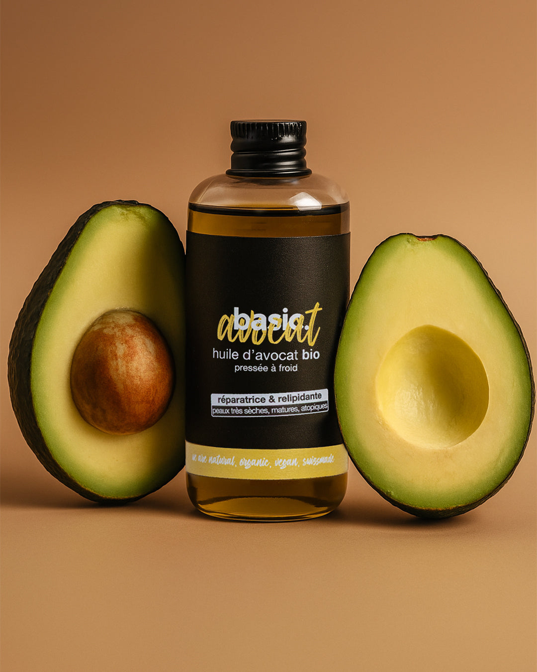 Flacon d'huile d'avocat bio Basic Cosmetics entouré d'avocats coupés