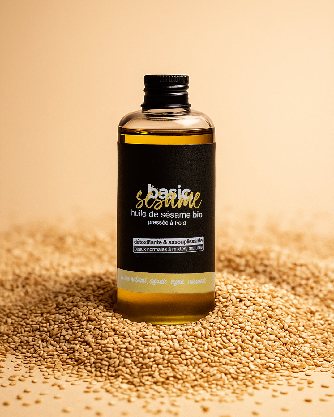 Flacon d'huile de sésame bio Basic Cosmetics posé sur des graines de sésame